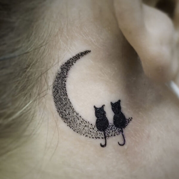 black tattoo of two cats sitting on a pointillism crescent moon