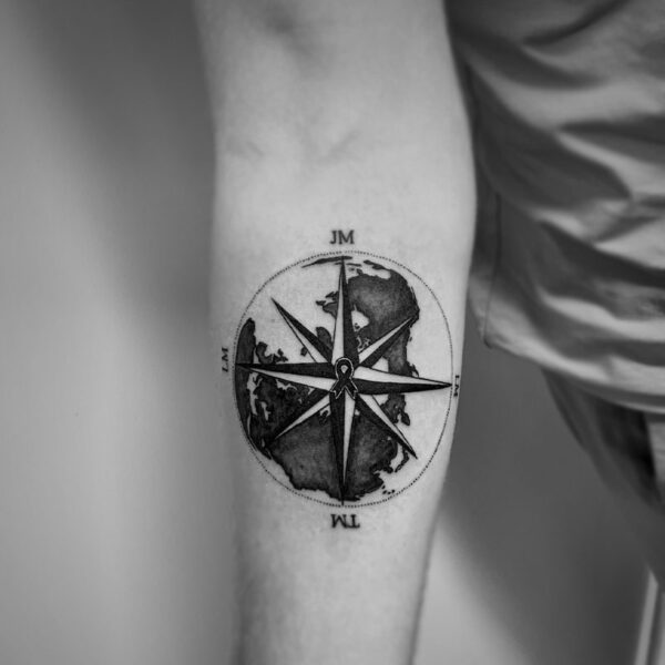 black and white tattoo of a compass over top the earth