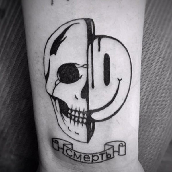 black and white tattoo of half a human skull and half a smiley face