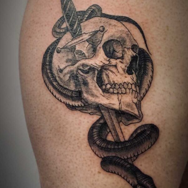 black and white tattoo of a human skull with a knife and snake