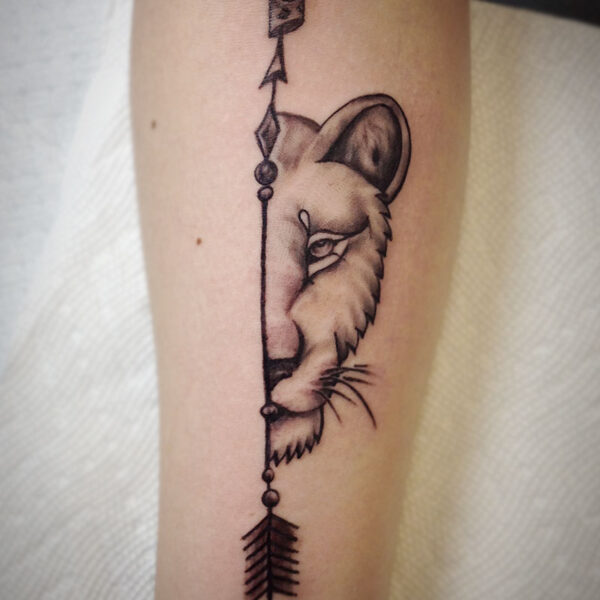 atticus tattoo, black and grey tattoo of half a lioness' face with a decorated arrow as the spilt down the middle