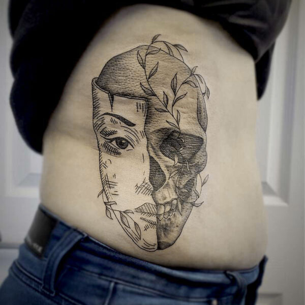 atticus tattoo, black and grey tattoo of a human skull wearing half a mask of a woman's face