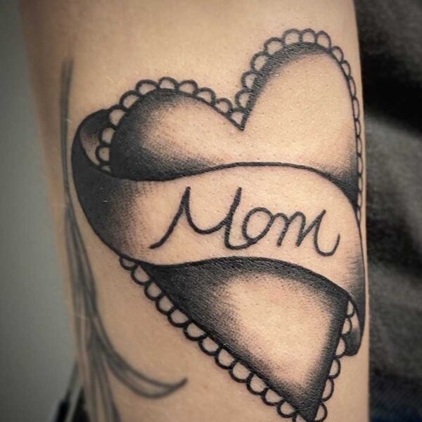 atticus tattoo, black and grey american traditional style tattoo of a heart with a ribbon that says mom