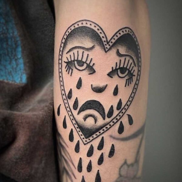 atticus tattoo, black and grey american traditional style tattoo of a heart with a woman's face that is crying