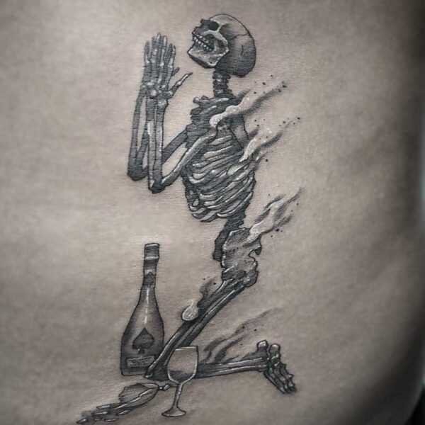 atticus tattoo, black and white tattoo of a skeleton praying with a bottle of wine and a glass beside it