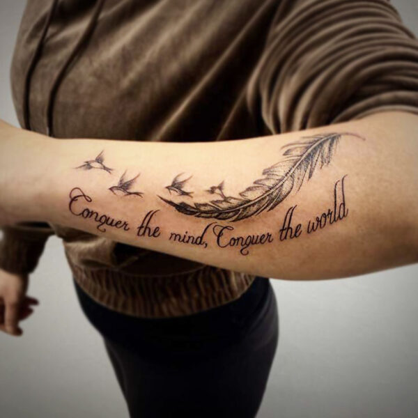 atticus tattoo, black and grey tattoo of birds flying from a feather and the words "conquer the mind; conquer the world"