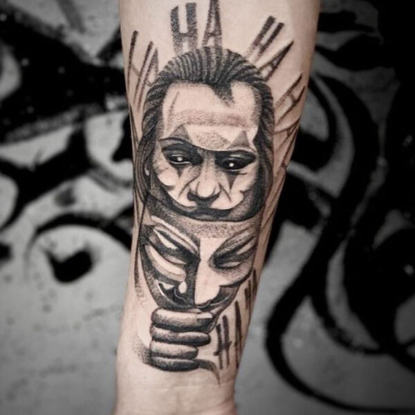 atticus tattoo, black and grey tattoo of the joker holding a Anonymous mask