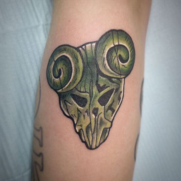 atticus tattoo, coloured neotraditional tattoo of a green wooden mask with ram horns