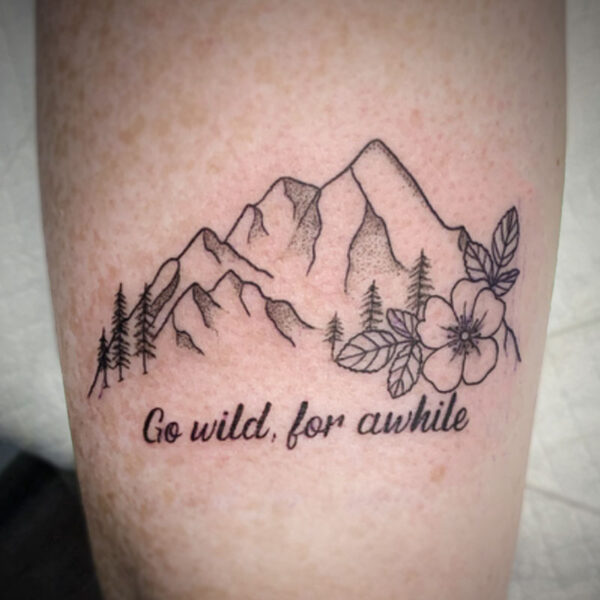 atticus tattoo, fine line tattoo of a mountain range, wild rose and the words "go wild, for awhile"