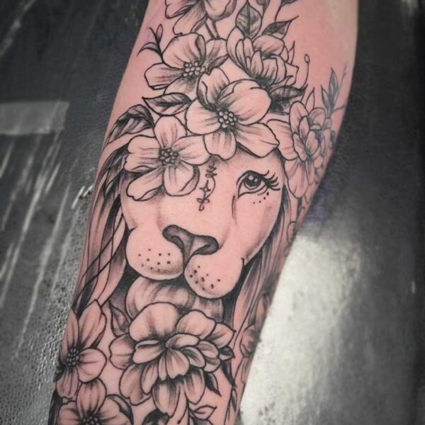 atticus tattoo, black and grey tattoo of a lion with flowers around it
