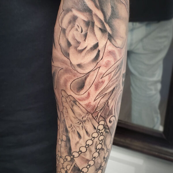 atticus tattoo, realism tattoo of a rose and hands praying with beads