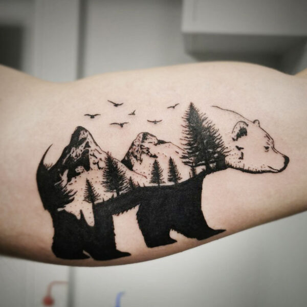 atticus tattoo, black tattoo of a bear with a mountain scene throughout its body