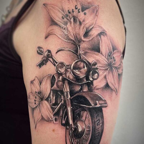atticus tattoo, black and grey realism tattoo of a Harley bike surrounded by lilies