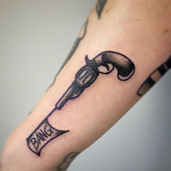 atticus tattoo, black and grey traditional tattoo of a pistol with a ribbon shooting out of it that says "bang"