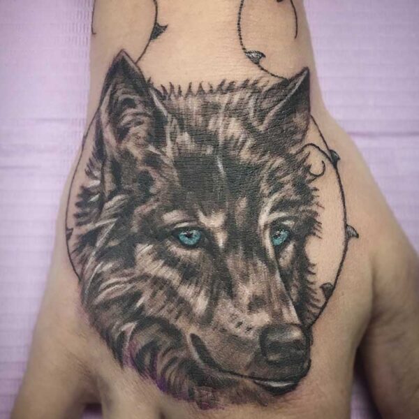 atticus tattoo, black and grey tattoo of a wolf with blue eyes and vines framing it