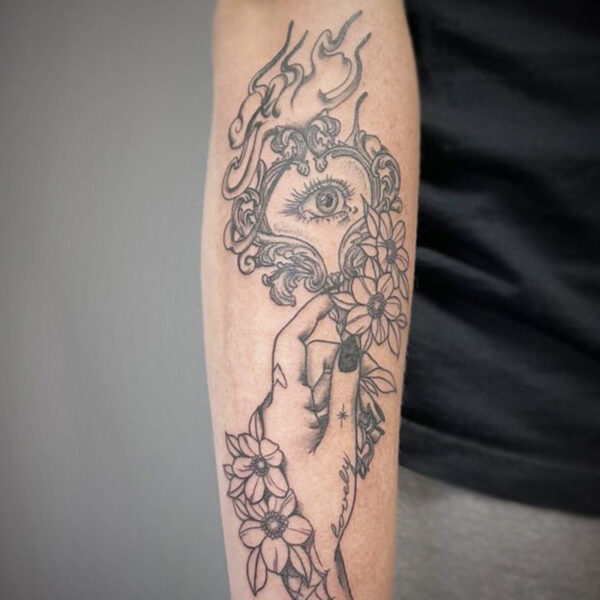 atticus tattoo, black and grey tattoo of a hand holding a decorated mirror with flowers