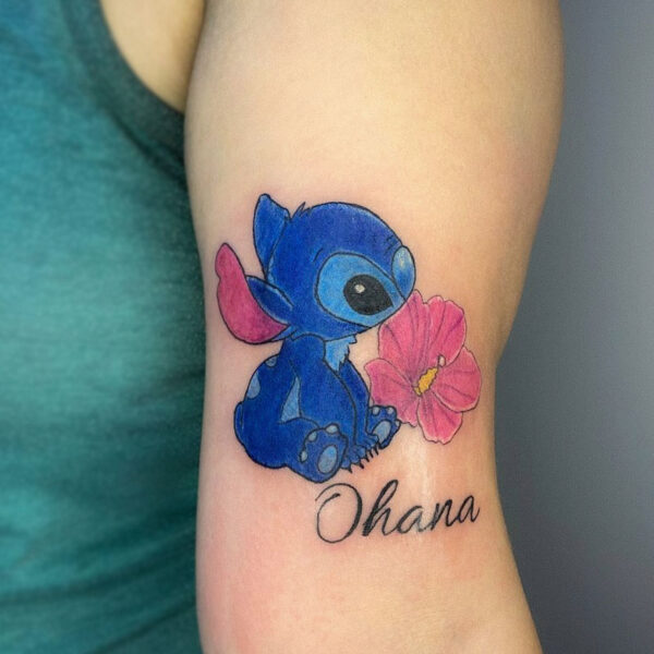 atticus tattoo, coloured tattoo of Stitch with a ink flower and the word "Ohana"
