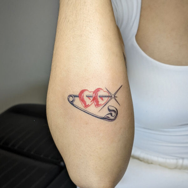 atticus tattoo, black and grey tattoo of a safety pin piercing two red hearts