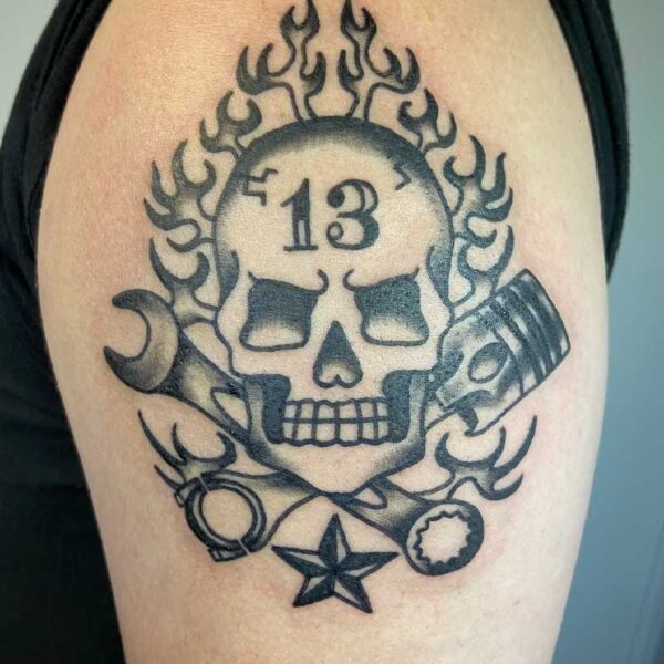 atticus tattoo; black and grey American traditional tattoo of a skull with flames, tools and the number 13