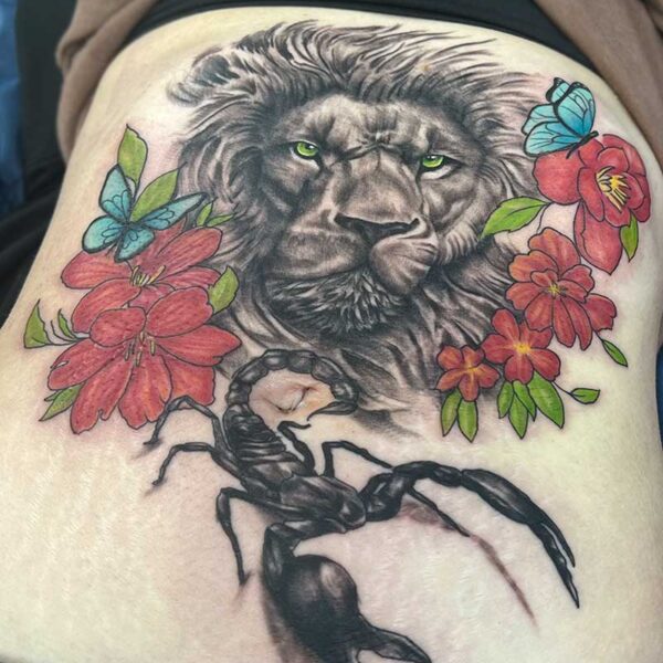 atticus tattoo; realism tattoo of a black and grey lion and scorpion with red flowers and blue butterflies