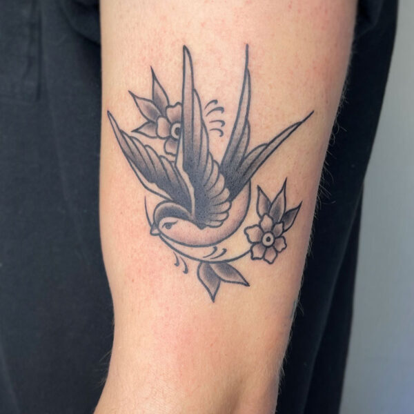 atticus tattoo, black and grey American traditional tattoo of a bird with flowers