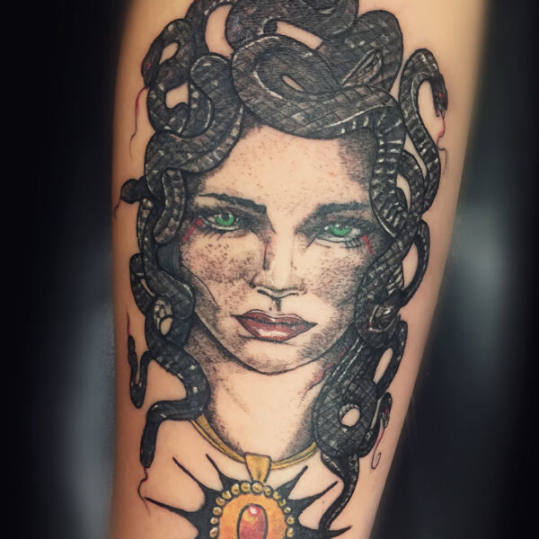 atticus tattoo, black and grey tattoo of Medusa with green eyes and an orange jewelled pendant