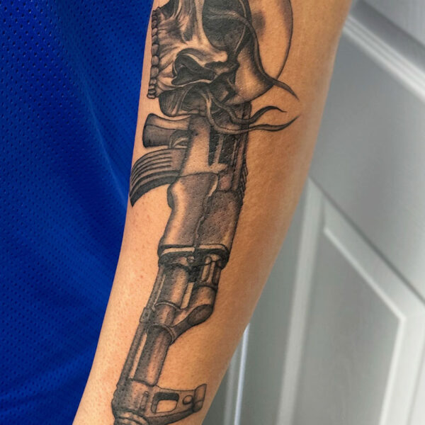 atticus tattoo, black and grey realism tattoo of a skull and looking through the scope of an assault rifle