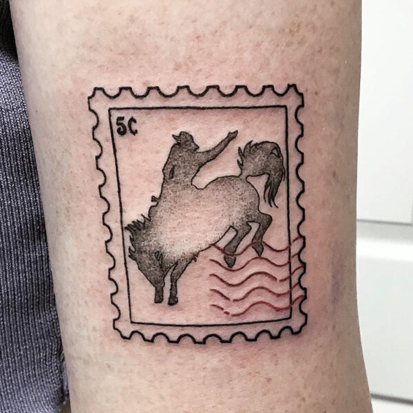 atticus tattoo, black and grey tattoo of a postage stamp with a cowboy and bucking horse silhouette