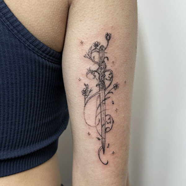 atticus tattoo, black and grey tattoo of a sword with flowers and swirls
