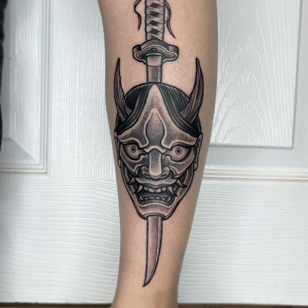 atticus tattoo, black and grey, neotraditional tattoo of an Oni mask with a katana going through it