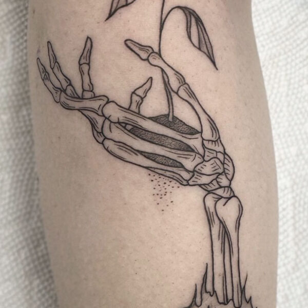 atticus tattoo, black and grey tattoo of a skeletons hand with a plant growing out of it