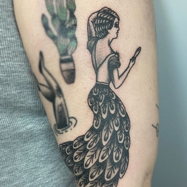 atticus tattoo, black and grey, American traditional tattoo of a woman in a peacock skirt