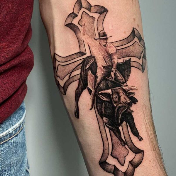 atticus tattoo, black and grey realism tattoo of a cross with a bull rider in front of it