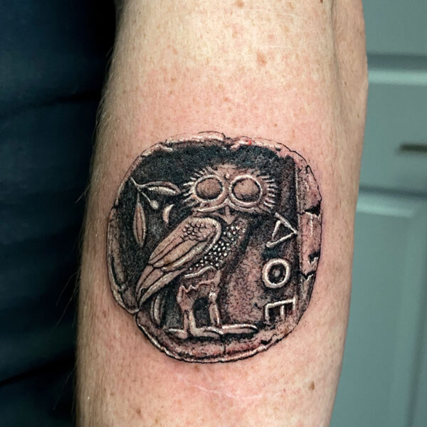 atticus tattoo, black and grey realism tattoo of an ancient coin with an owl on it