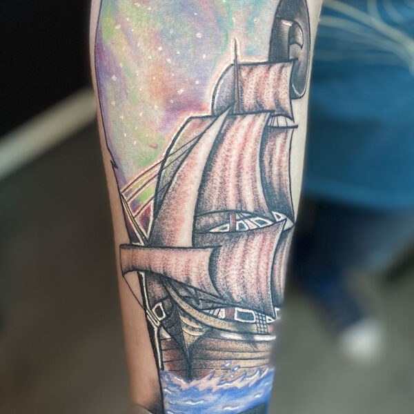 atticus tattoo, neotraditional tattoo of a sailing ship with a scroll in the background and the Northern lights in the scroll