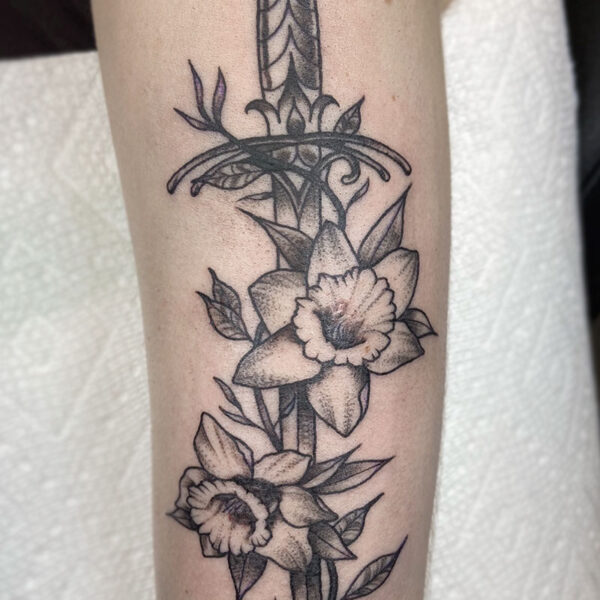 atticus tattoo, black and grey tattoo of a dagger with daffodils