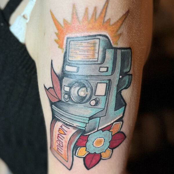 atticus tattoo, neotraditional tattoo of a Polaroid camera, flowers and a a picture printing that says "memories"