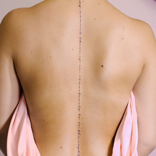 atticus tattoo, fine line tattoo of script down the center of a woman's back