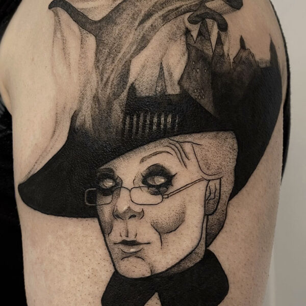 atticus tattoo, black and grey tattoo of Professor McGonagall from Harry Potter, with a scene of Hogwarts on her hat and smoky cat jumping over it