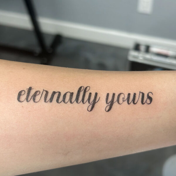 atticus tattoo, black script tattoo of the words "eternally yours"