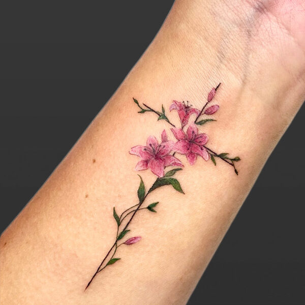 Tattoo of a small cross with pink lilies and green vines