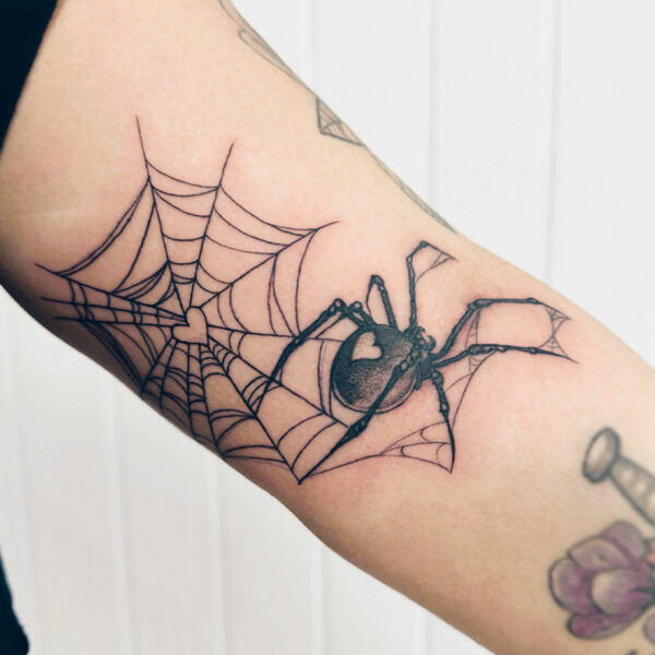 Black and grey tattoo of a spider and web, both with a heart in the centre
