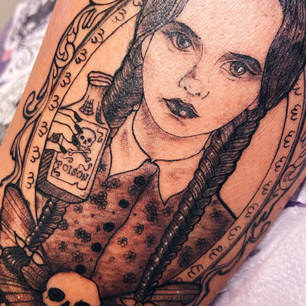 Black and grey tattoo of Wednesday Addams framed with roses and a death skull moth