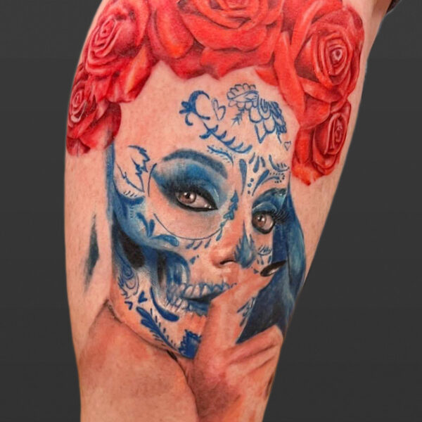 Atticus Tattoo| Colour realism tattoo of a woman with blue, sugar skull face paint and red roses on her head