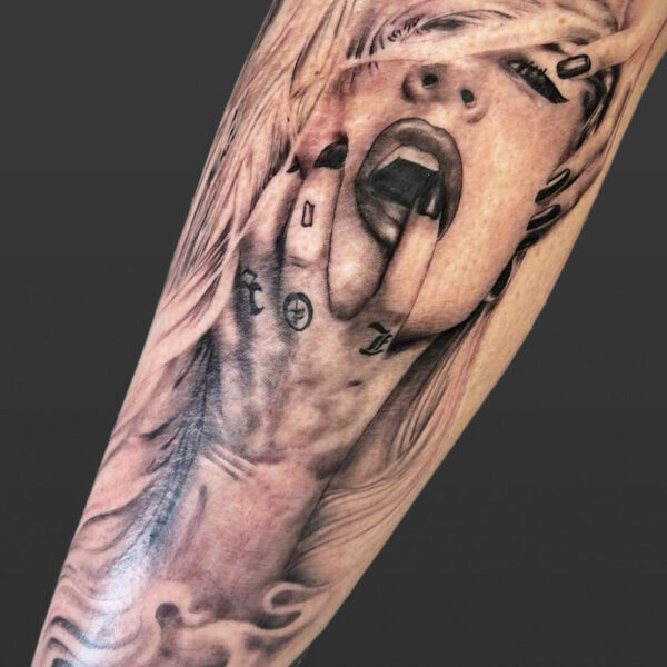 Atticus Tattoo| Black and grey, realism tattoo of a blonde woman, holding her head with one hand and holding her open mouth with her other hand that has small tattoos