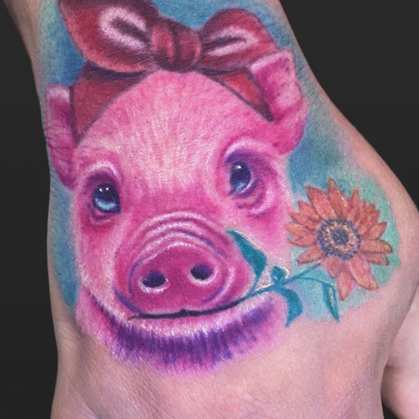 Atticus Tattoo| Colour realism tattoo of a pink piglet holding a flower in it's mouth and wearing a red bow