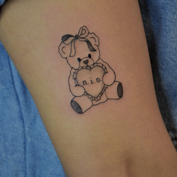Atticus Tattoo| Fine line tattoo of a teddy bear with ribbon and holding a heart