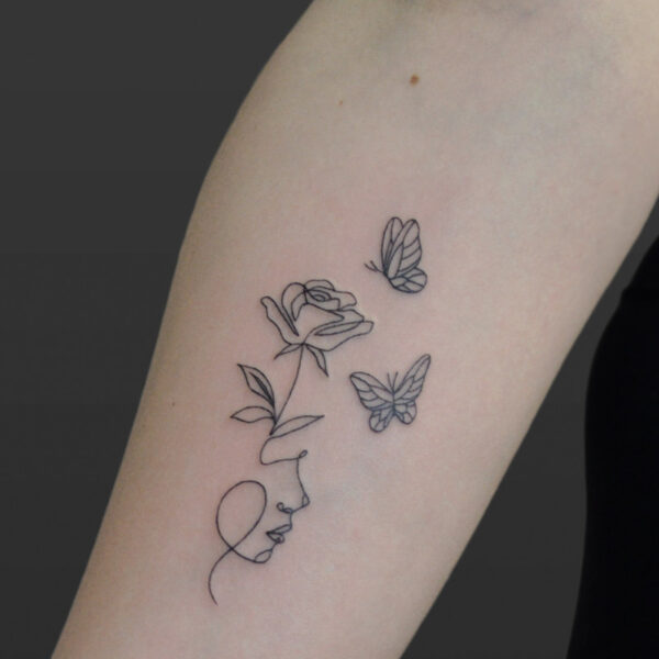Atticus Tattoo| Fine line tattoo of the outline of a woman's face with a rose and butterflies