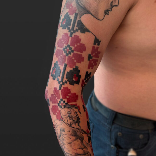 Atticus Tattoo| Ukrainian themed sleeve tattoo, with red and black flowers, a viking man and a woman with red poppies in her hair