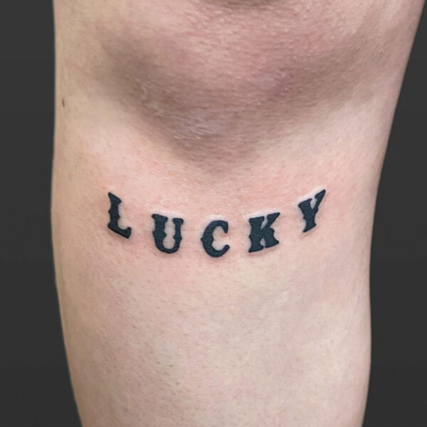 Atticus Tattoo| Blackwork, script tattoo of the word "Lucky"